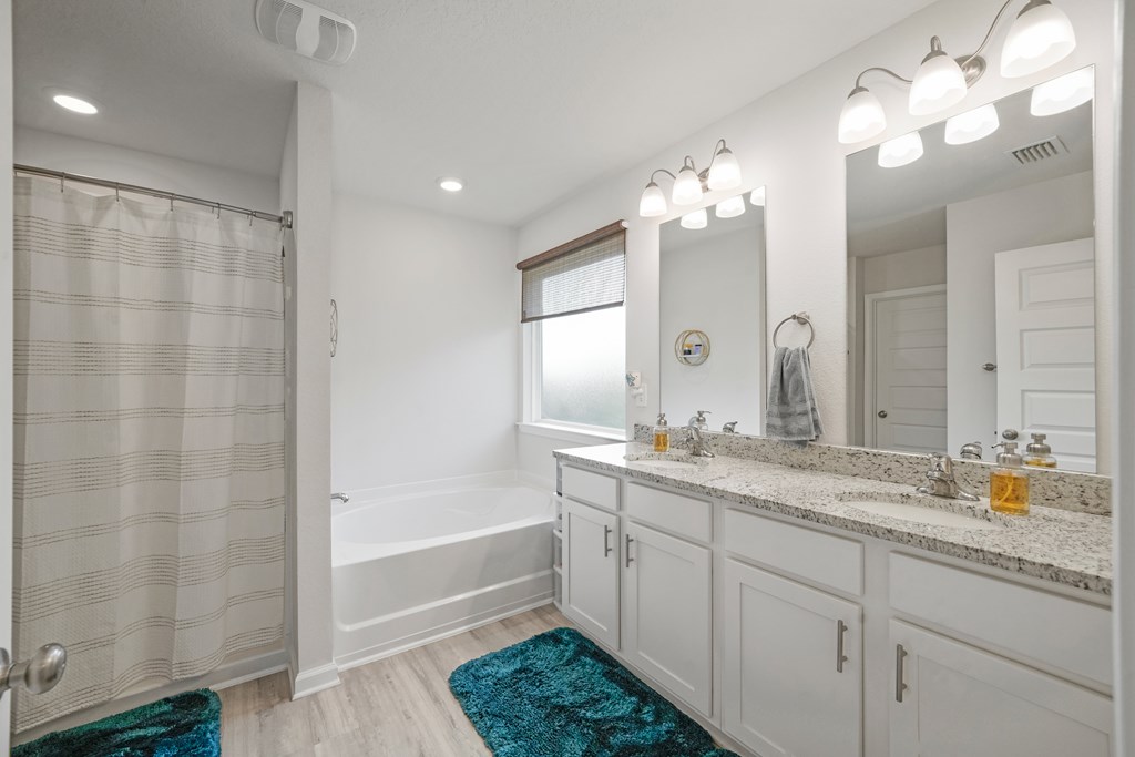 Bathroom with a long double vanity, stone countertop, bathtub, and striped shower curtain.