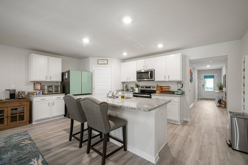 Kitchen with white cabinets, a granite island, two bar chairs, and a pale green refrigerator.