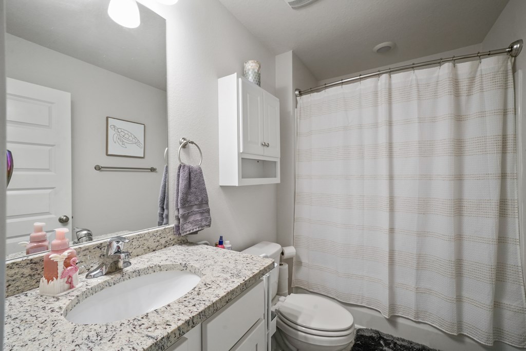 Bathroom with a granite vanity, oval sink, and white striped shower curtain.