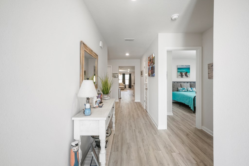 Hallway with light wood-look floors and a console table, looking toward a bedroom with a turquoise bedspread.