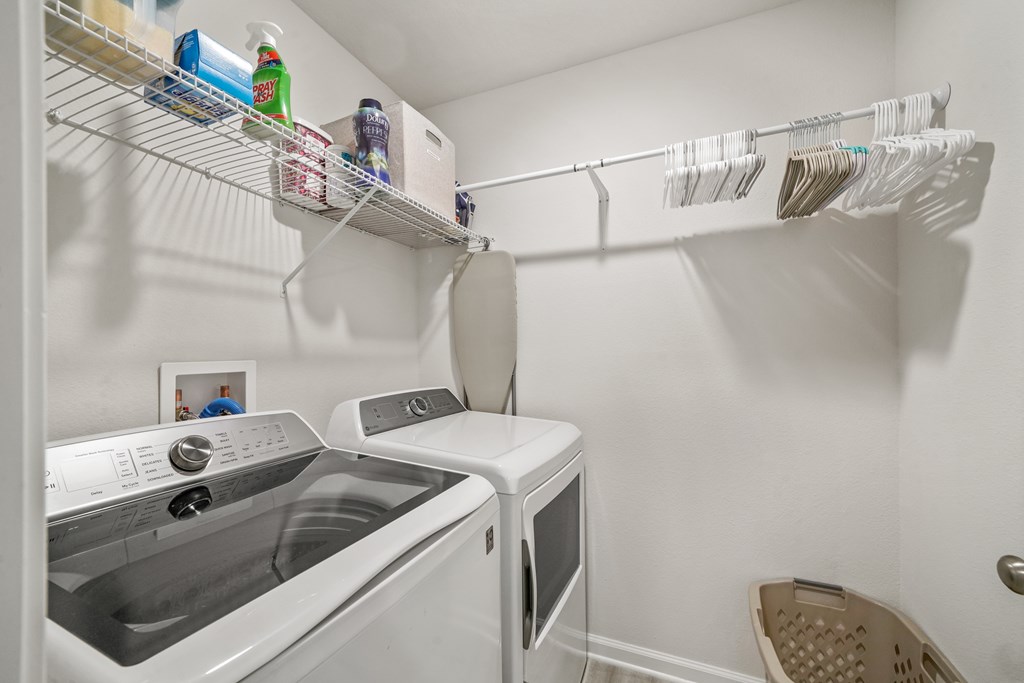 Laundry room with washer and dryer beneath wire shelving and a rod of clothes hangers.