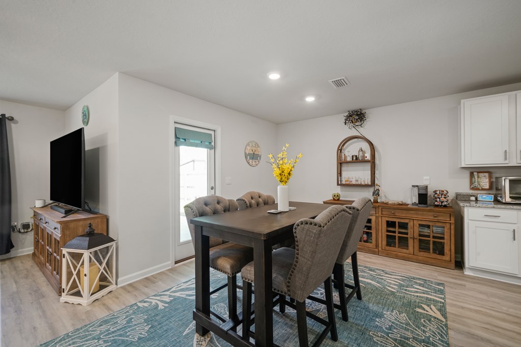 Dining area with a dark table, gray upholstered chairs, and a patterned blue rug beside the kitchen.