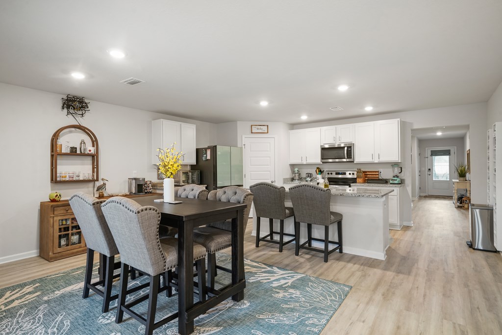 Open kitchen and dining area with a white island, stainless appliances, and a dark table on a blue rug.