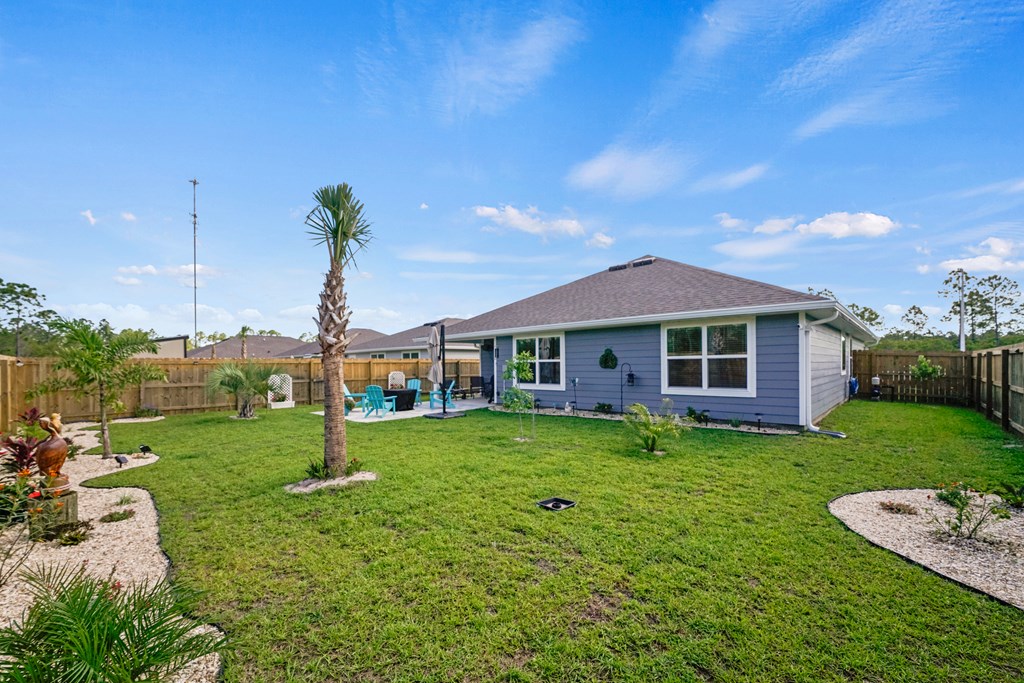 Home’s rear exterior with a fenced lawn, palm trees, and patio seating.