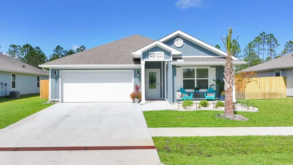 Blue-gray house with a white double garage, turquoise porch chairs, and a palm tree by the driveway.