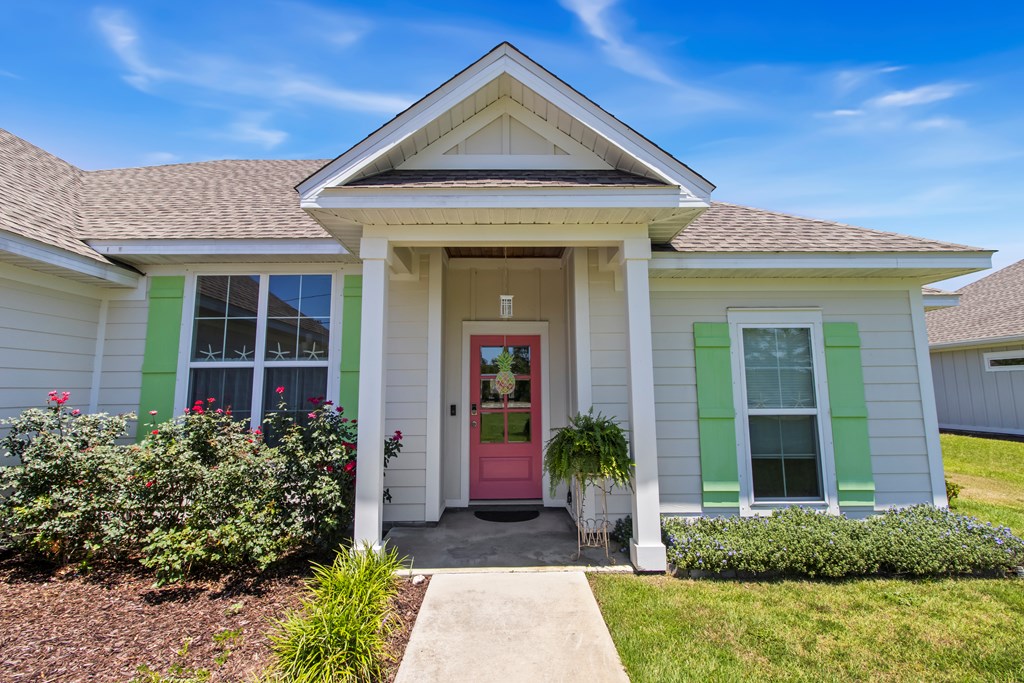 House front with a peaked portico, pink door, green shutters, and landscaped flower beds.