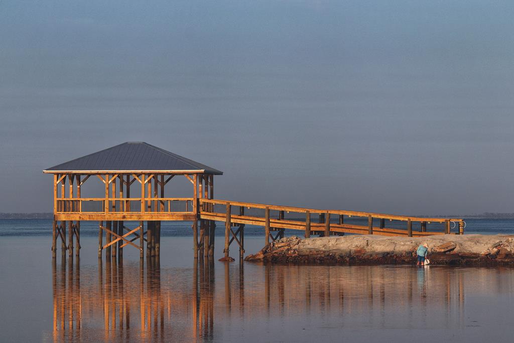 Covered wooden pier and ramp over calm water, with a rocky shoreline and reflections.