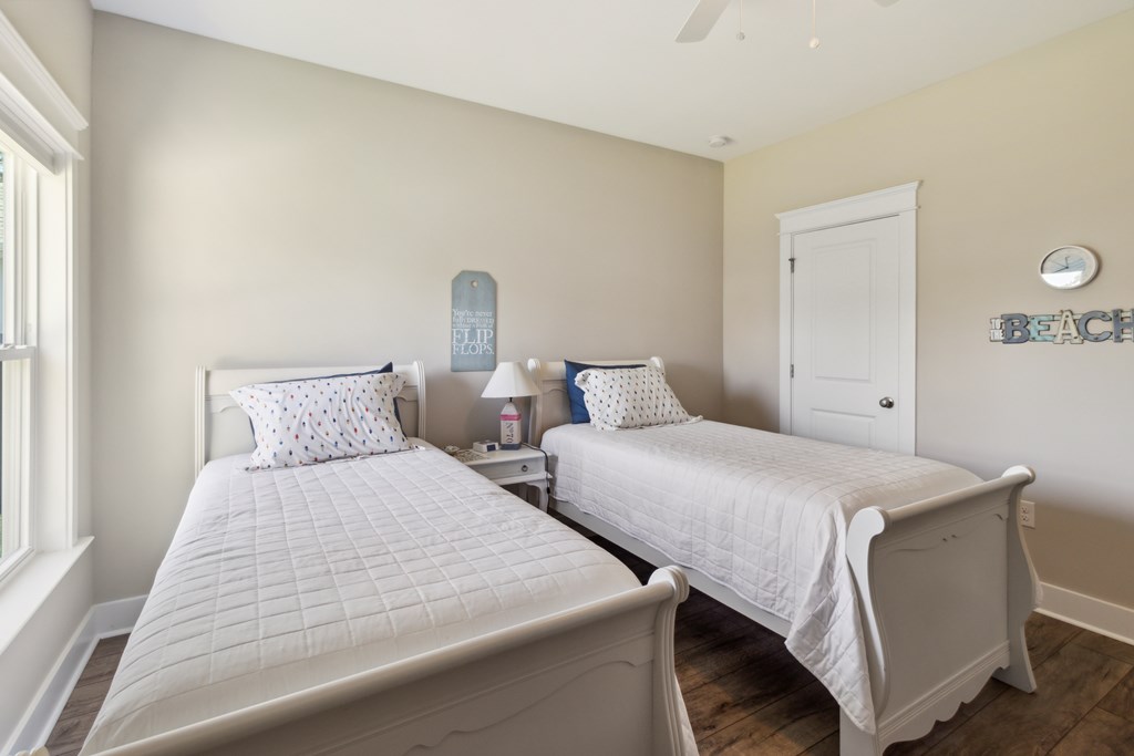 Bedroom with two white twin beds, beach-themed wall decor, and dark wood flooring.