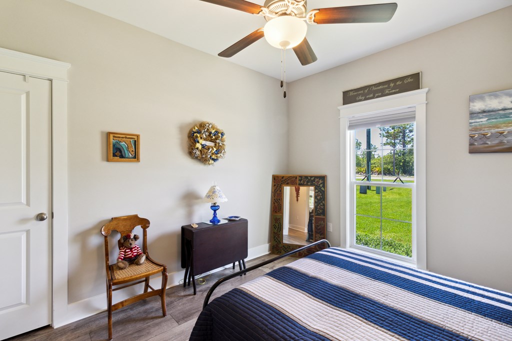 Bedroom with a blue-and-white striped bedspread, ceiling fan, and large window overlooking a lawn.