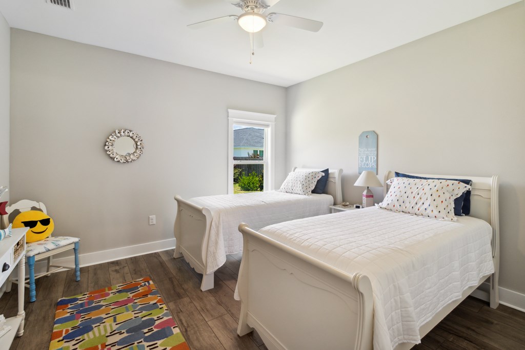 Bedroom with two white beds, patterned pillows, and a colorful rug on dark wood-look flooring.