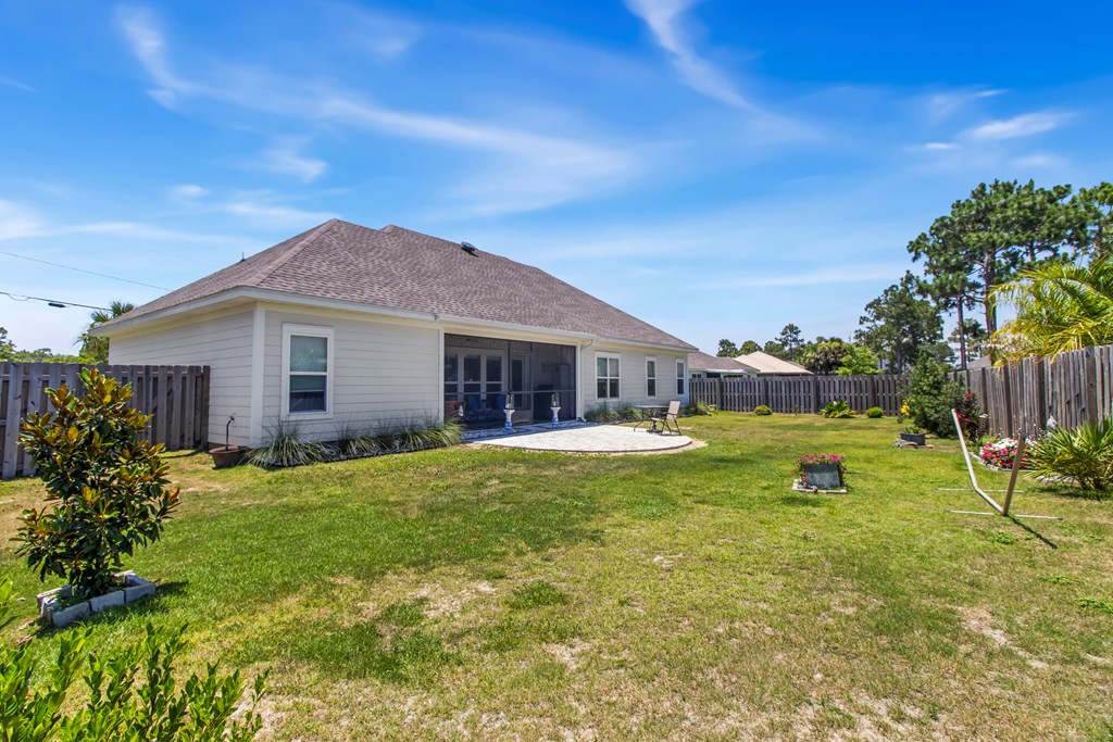 Home’s rear exterior and fenced backyard with a small patio, lawn, and flower beds.