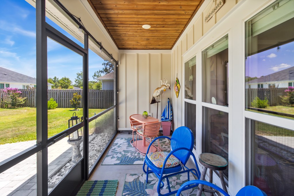 Screened porch with a wood ceiling, colorful seating, and views of a fenced backyard.