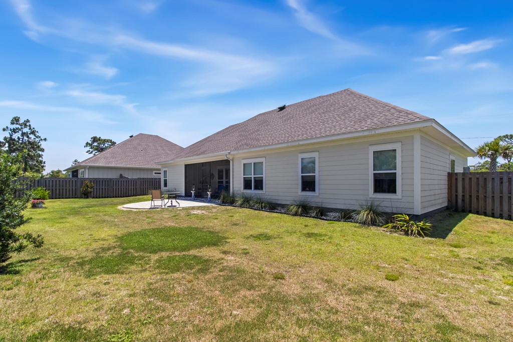 Rear of a single-story home with a covered patio and fenced grassy backyard.