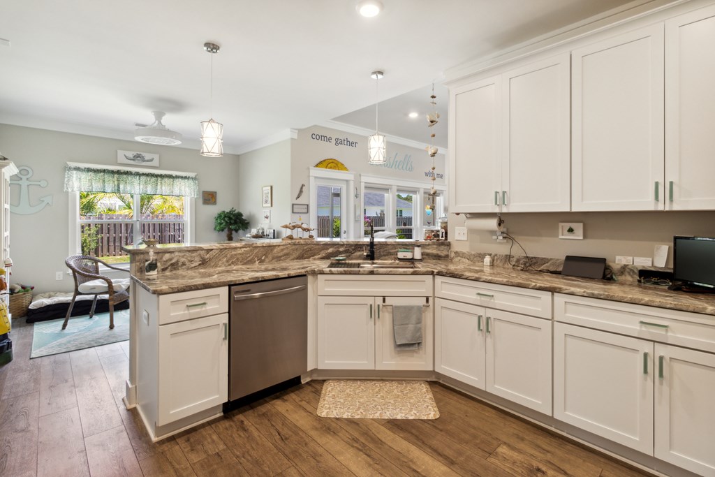 Kitchen with white shaker cabinets, an L-shaped stone counter, and stainless steel dishwasher.