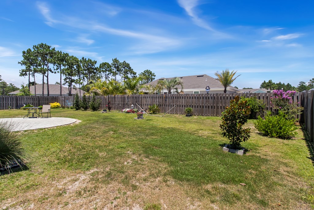 Backyard lawn bordered by a wooden privacy fence, with landscaped shrubs and a curved patio.