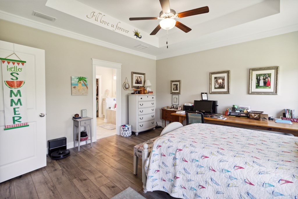Bedroom with a wood-look floor, ceiling fan, and long desk beside the bed.