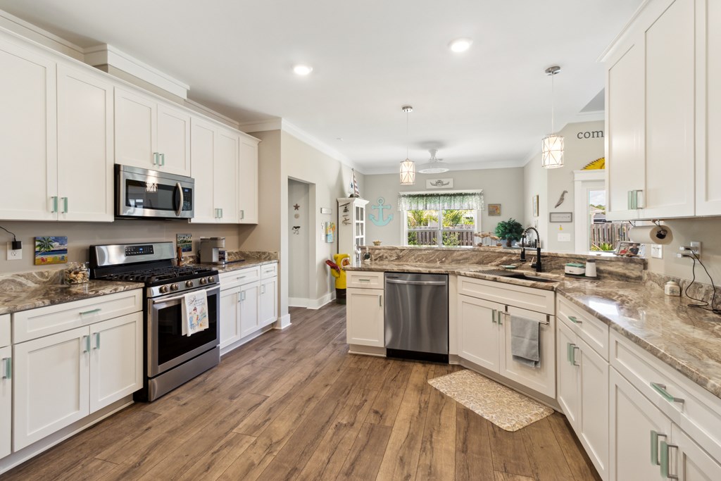 Open kitchen with white cabinetry, a large stone island, and stainless steel appliances.