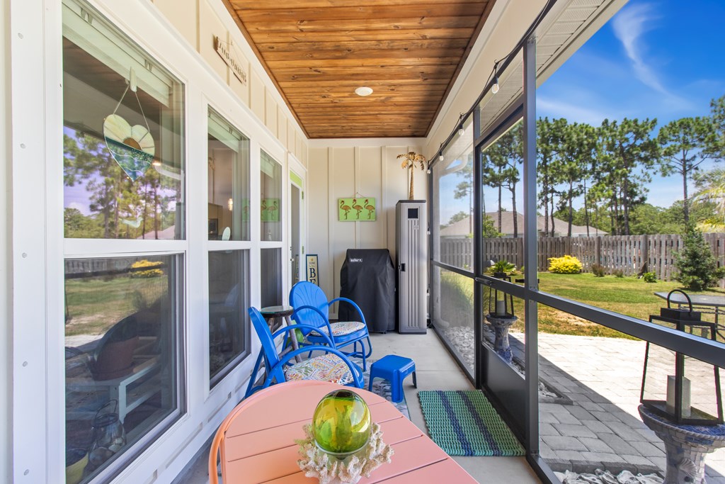 Screened porch with blue chairs, a wood-plank ceiling, and views of the fenced yard.