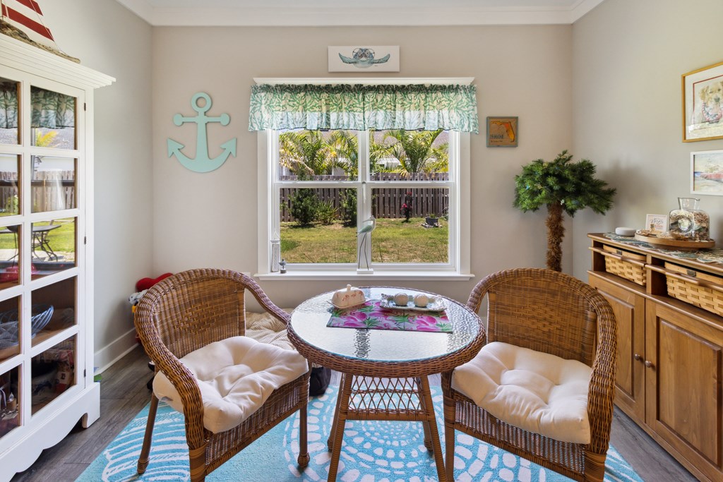 Furnished sunroom with wicker chairs, a round table, and a large window overlooking a fenced yard.