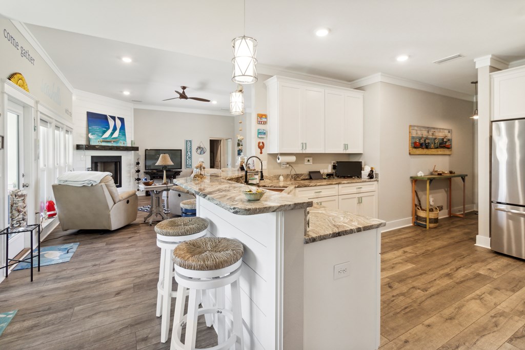Open-plan kitchen with a large granite island, white cabinets, and breakfast stools beside the living area.