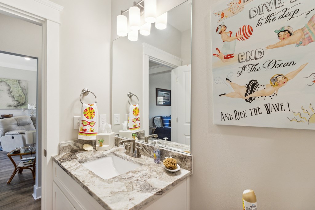 Bathroom vanity with a mottled stone countertop, large mirror, and colorful ocean-themed poster.
