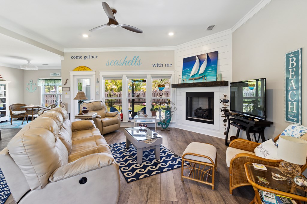 Furnished coastal living room with cream sofas, a white fireplace, sailboat artwork, and garden-facing glass doors.