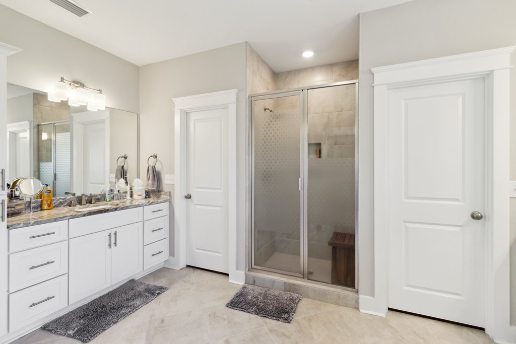 Bathroom with a white double vanity and glass-enclosed tiled shower.