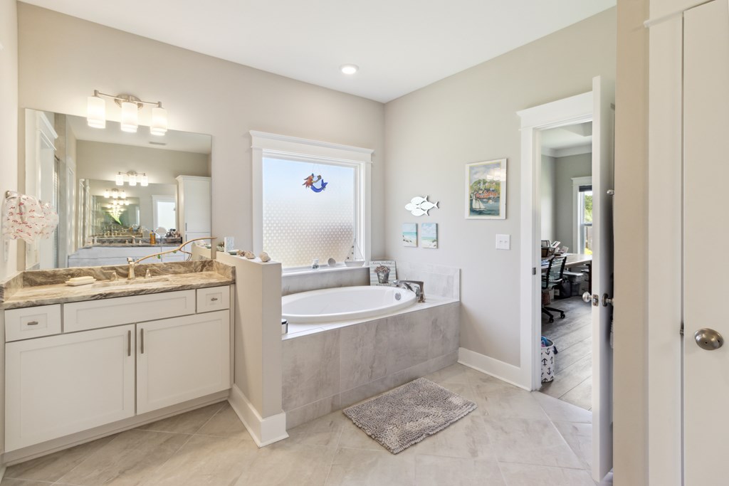 Bathroom with a soaking tub beneath a patterned shade and a white vanity with a stone-look countertop.