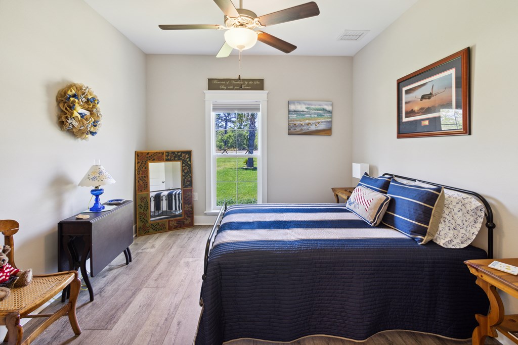 Furnished bedroom with navy striped bedding, a ceiling fan, and a window overlooking a lawn.