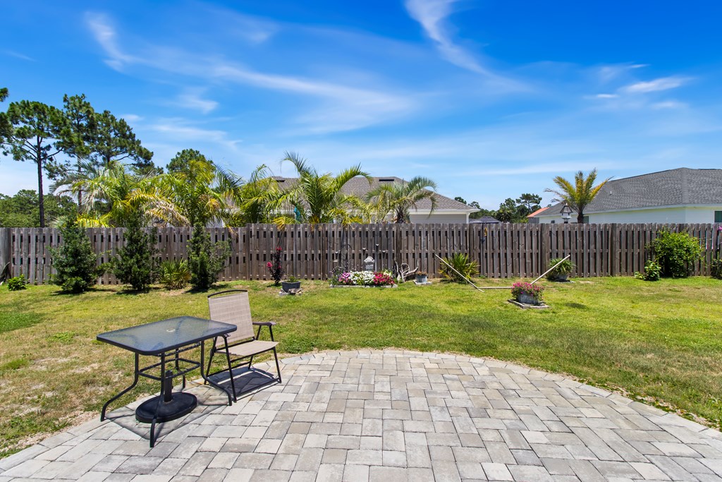 Backyard patio with pavers, outdoor table and chair, lawn, and wooden privacy fence.