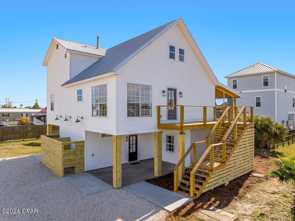 White elevated house with a metal roof, raised wooden deck, and long exterior staircase.