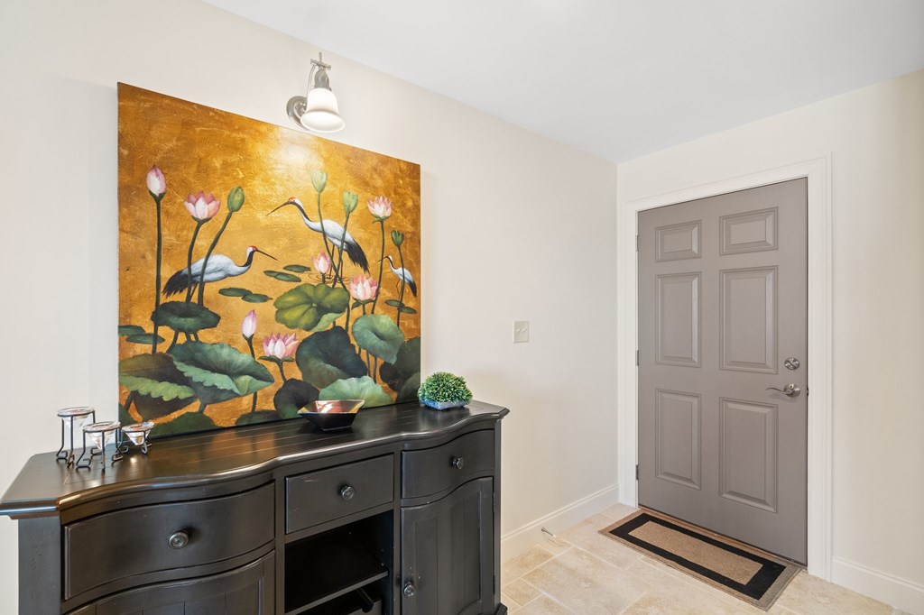 Condominium entryway with a gray paneled door, tiled floor, and dark console beneath bird-and-water-lily artwork.