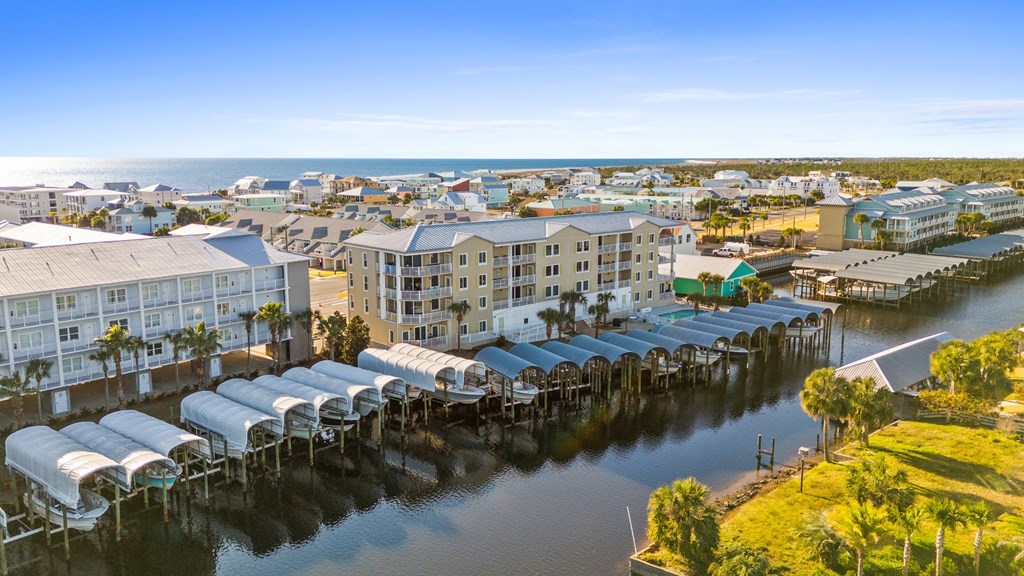 Waterfront condominium buildings and covered boat slips beside a canal, with the Gulf in the distance.