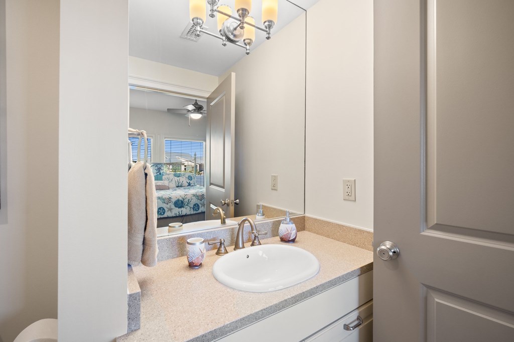 Bathroom vanity with an oval sink and large mirror reflecting a blue-and-white bedroom.