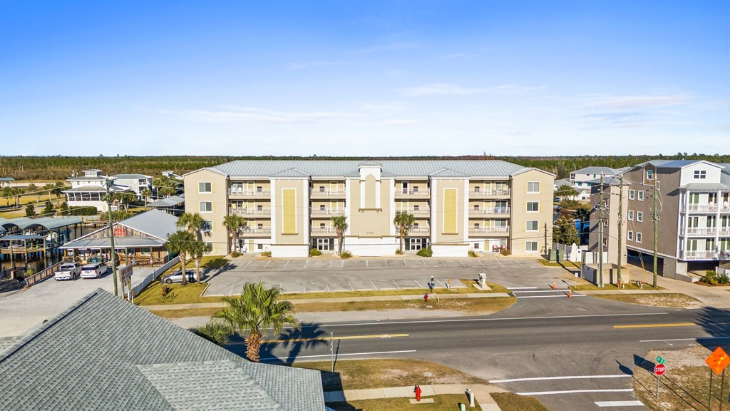 Condominium building with rows of balconies and a large parking lot across the road.