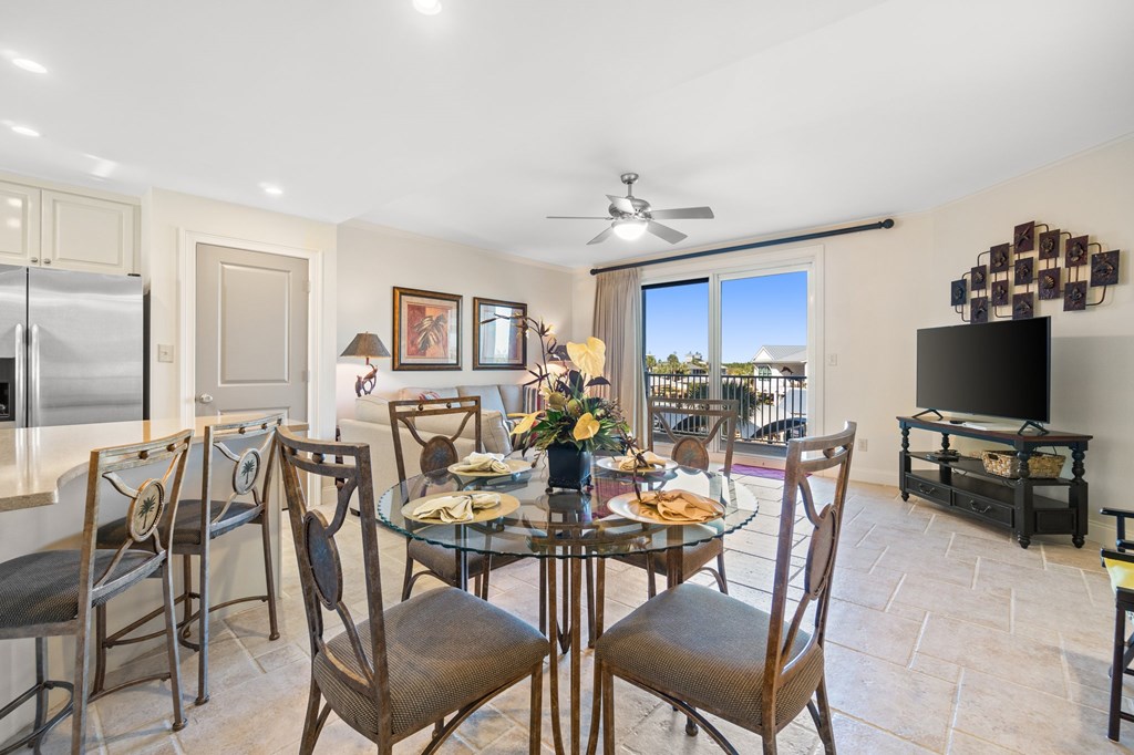 Condo dining area with a glass table, kitchen bar, and sliding doors opening onto a balcony.