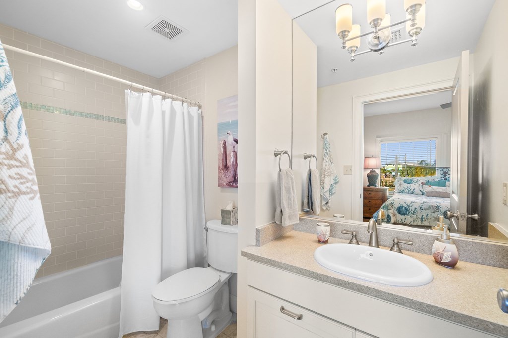 Bathroom with tiled tub and shower, white vanity, and a view into a tropical-patterned bedroom.
