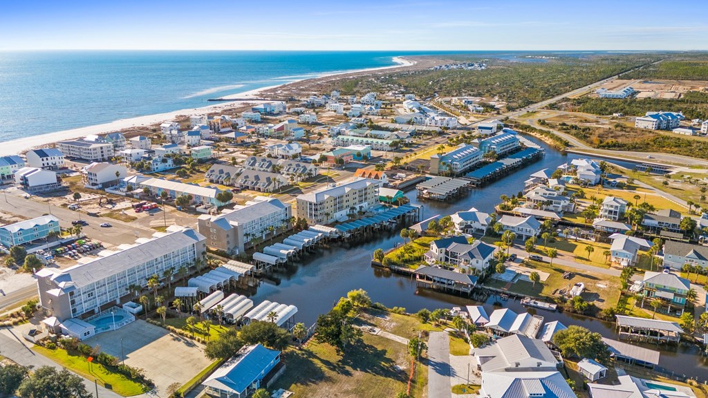 Aerial coastal neighborhood with a canal, waterfront homes, docks, and the Gulf beach beyond.