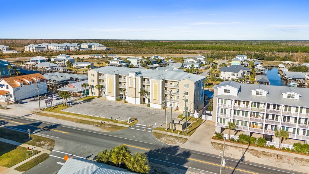 Aerial view of coastal condominiums beside a road, with a canal and homes nearby.