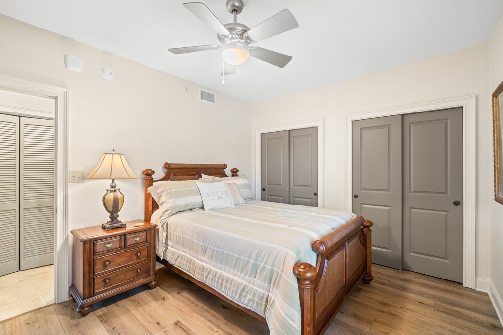 Furnished bedroom with a wooden bed, striped bedding, bedside lamp, and gray closet doors.