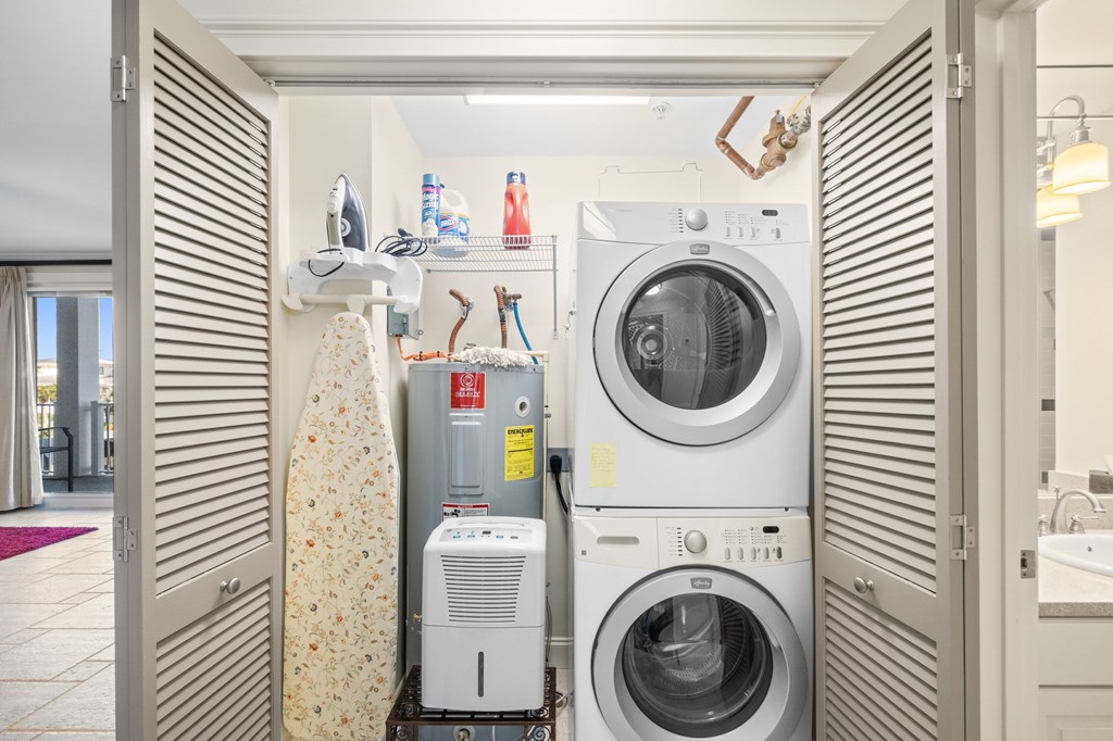Laundry closet with stacked washer and dryer, ironing board, and water heater.