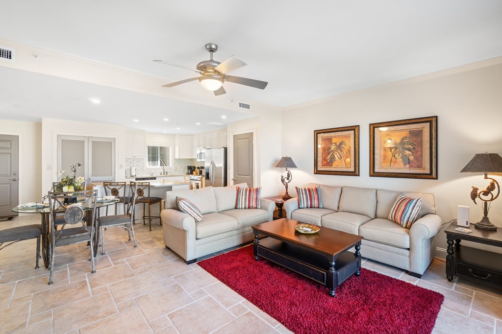 Furnished condo living room with a light sectional, red rug, and open dining area and kitchen.