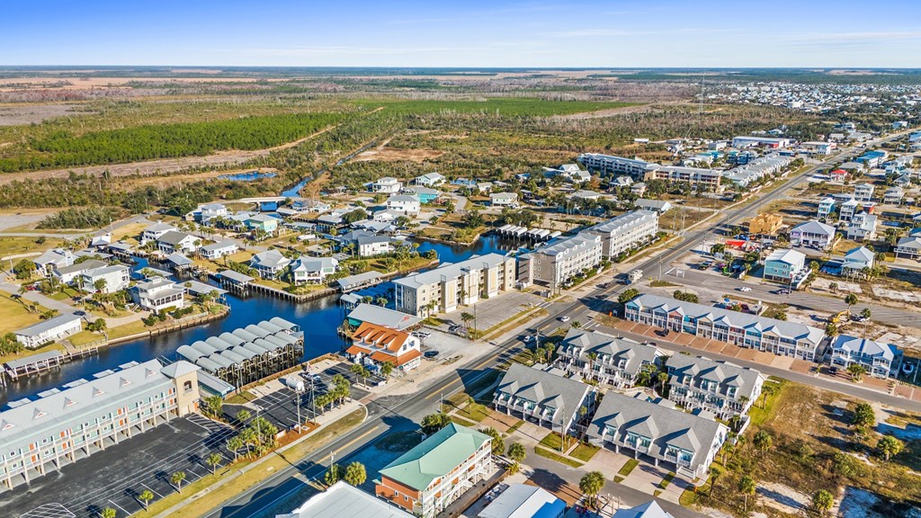 Aerial view of coastal condos, canal-side homes and docks, with open water on the horizon.