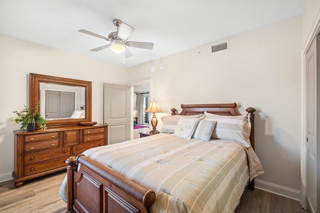 Furnished bedroom with a wooden bed, striped bedding, matching dresser, and ceiling fan.