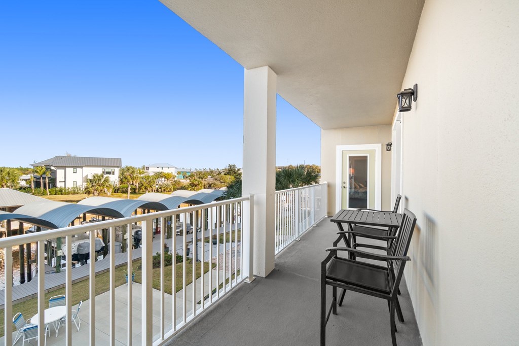 Condo balcony with two black chairs and a table overlooking landscaped grounds and covered parking.