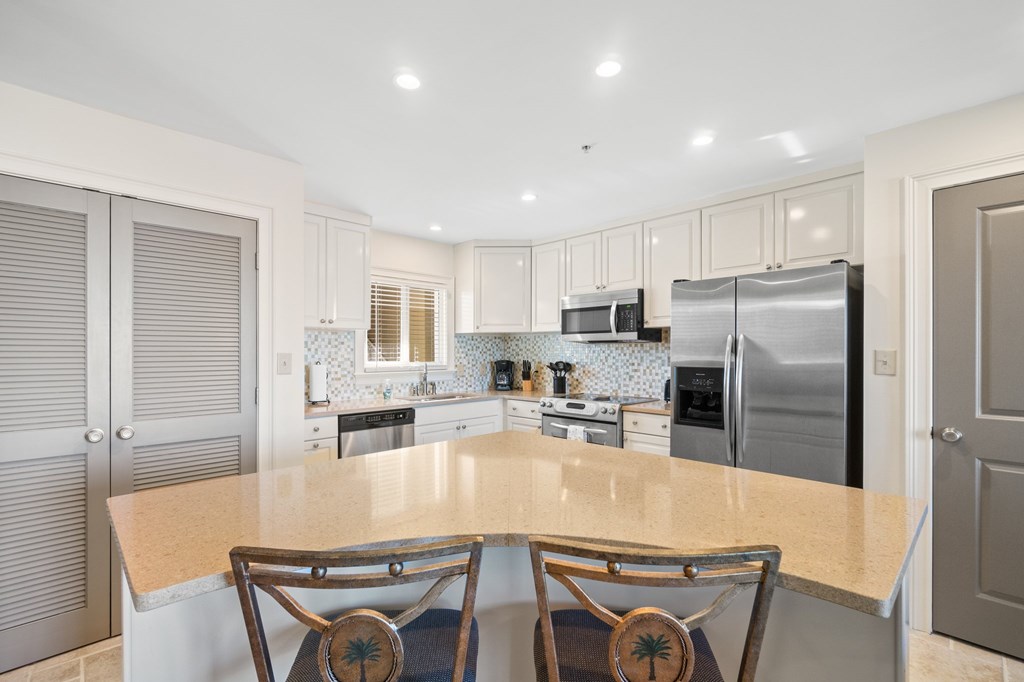 Kitchen with a large peninsula, two bar stools, stainless steel appliances, and a mosaic tile backsplash.