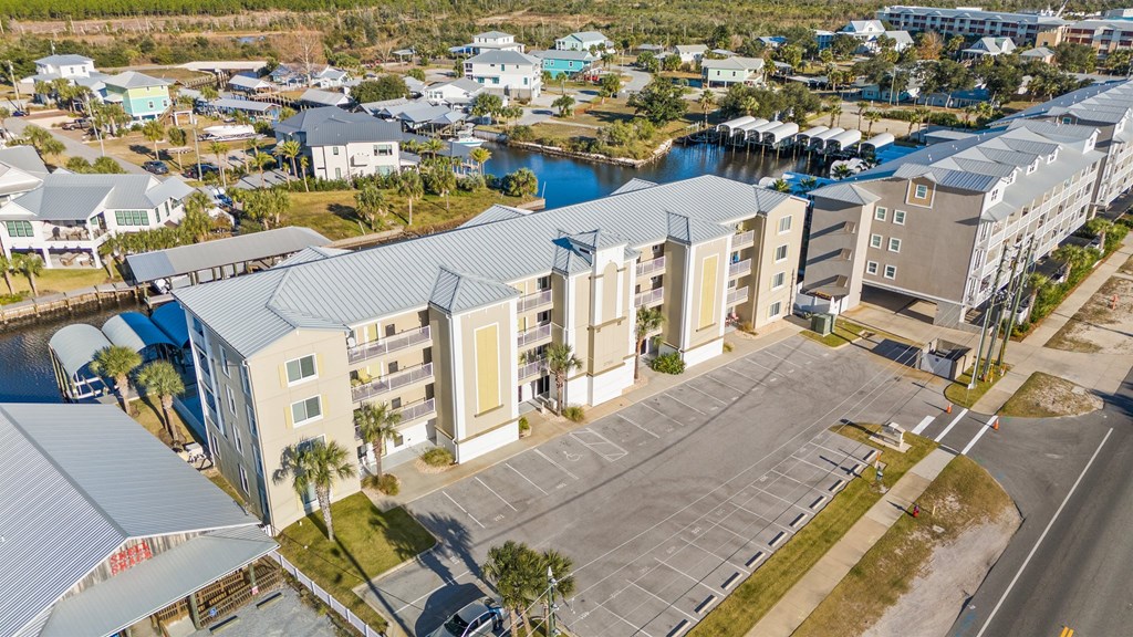 Aerial view of a coastal condominium complex beside a canal, with boat slips and a large parking lot.