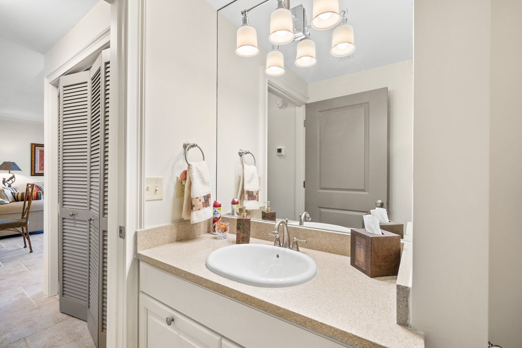 Bathroom vanity with an oval sink, beige countertop, large mirror, and chrome light fixtures.