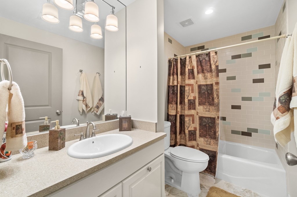 Bathroom with a long vanity, large mirror, and tiled tub-shower with a patterned curtain.