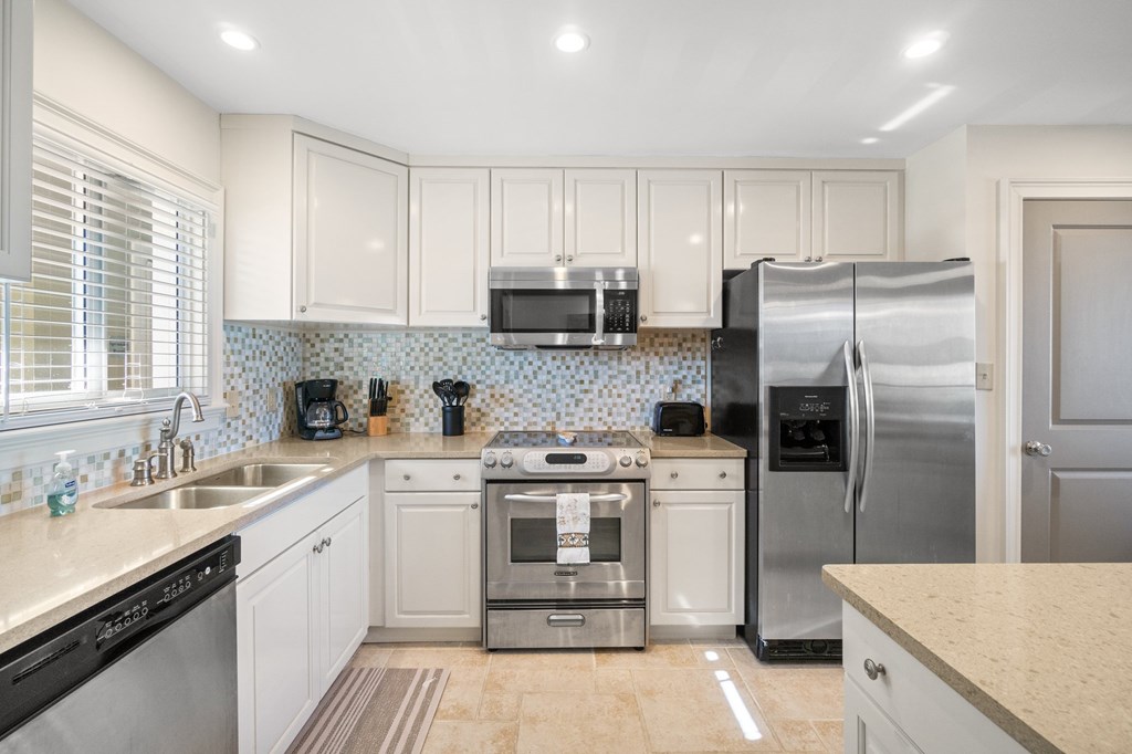 Condo kitchen with white cabinets, stainless steel appliances, mosaic backsplash, and window over the sink.